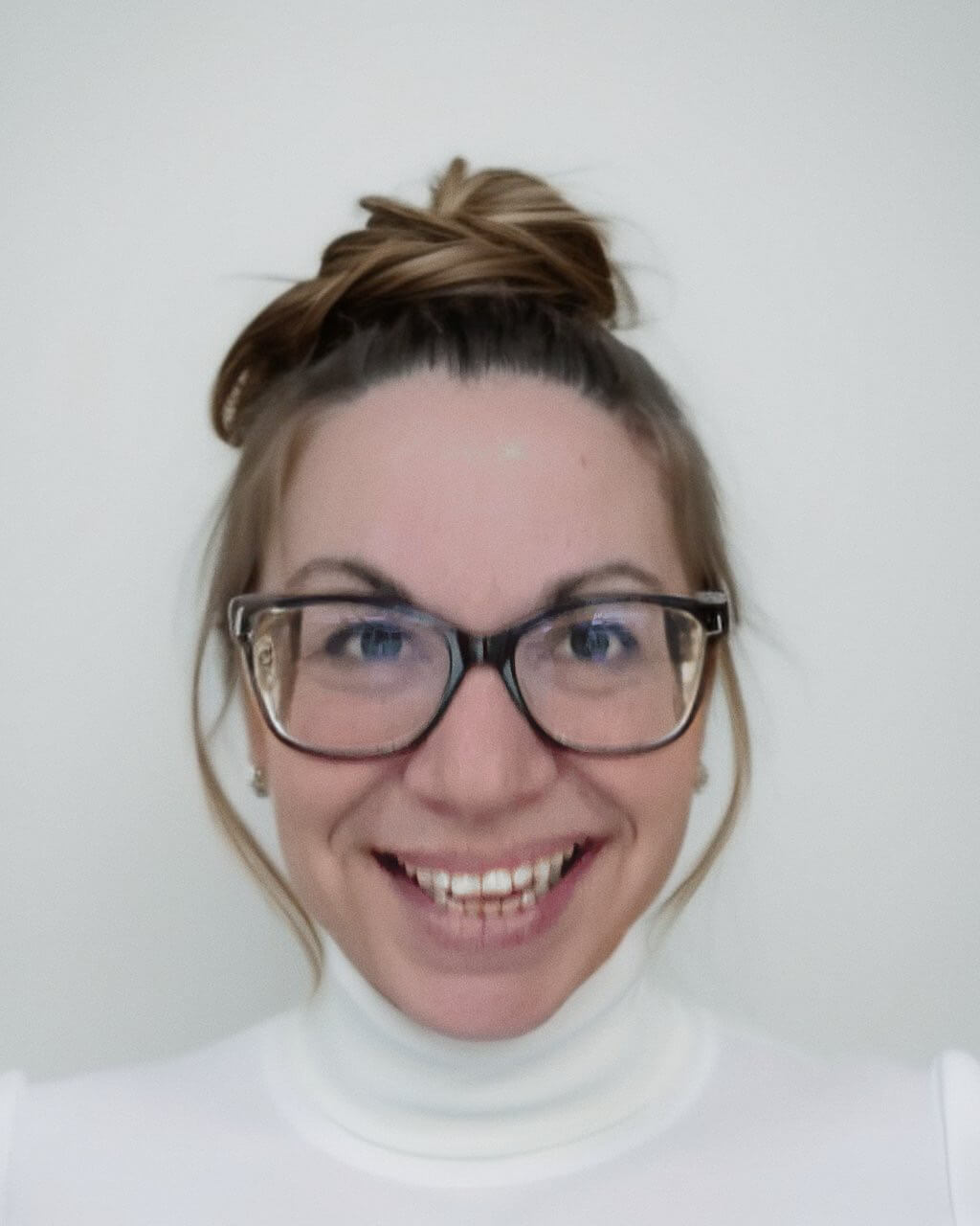 a white woman with a white turtle neck, hair in bun, and glasses