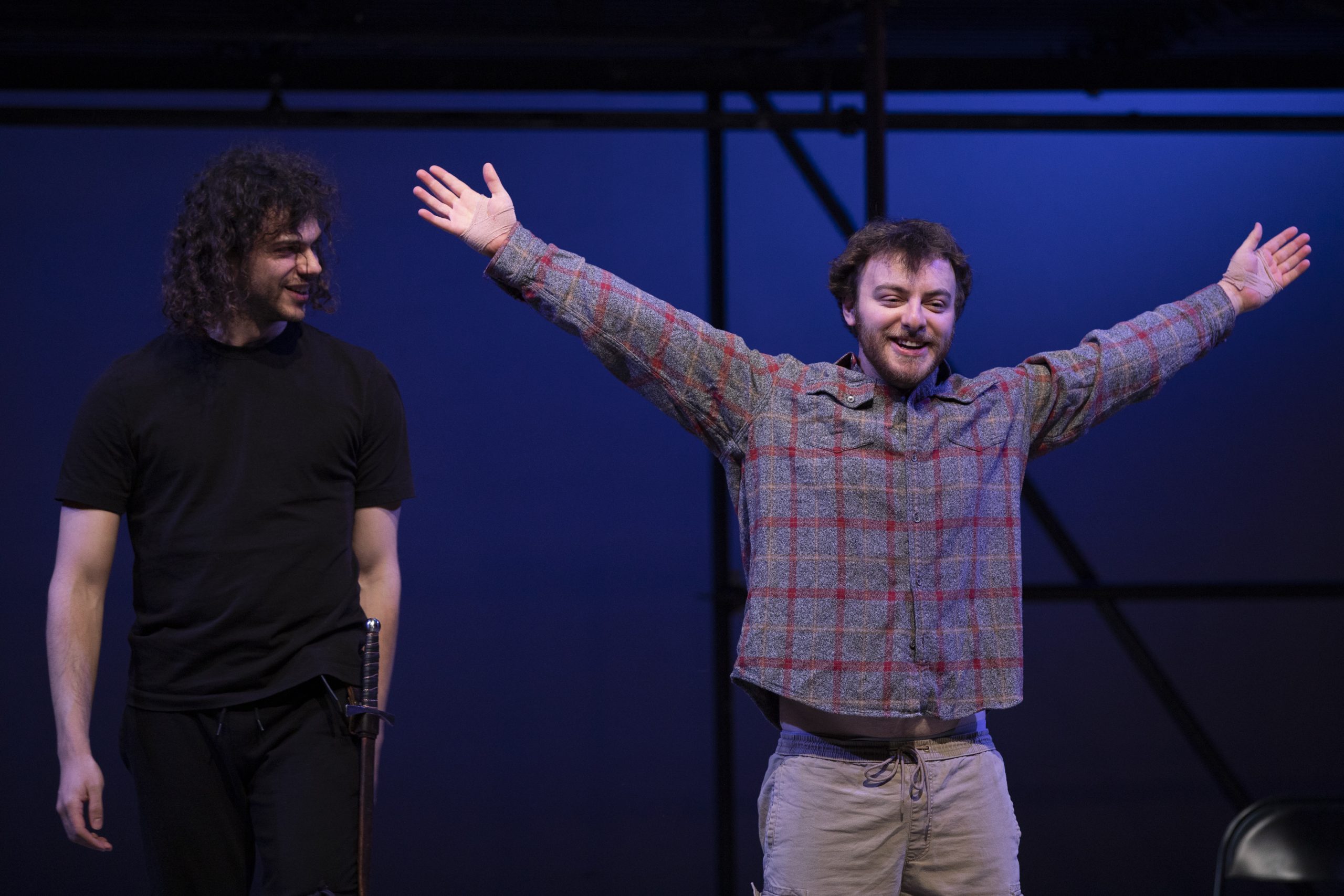 A man in a plaid shirt on a stage with his arms outstretched
