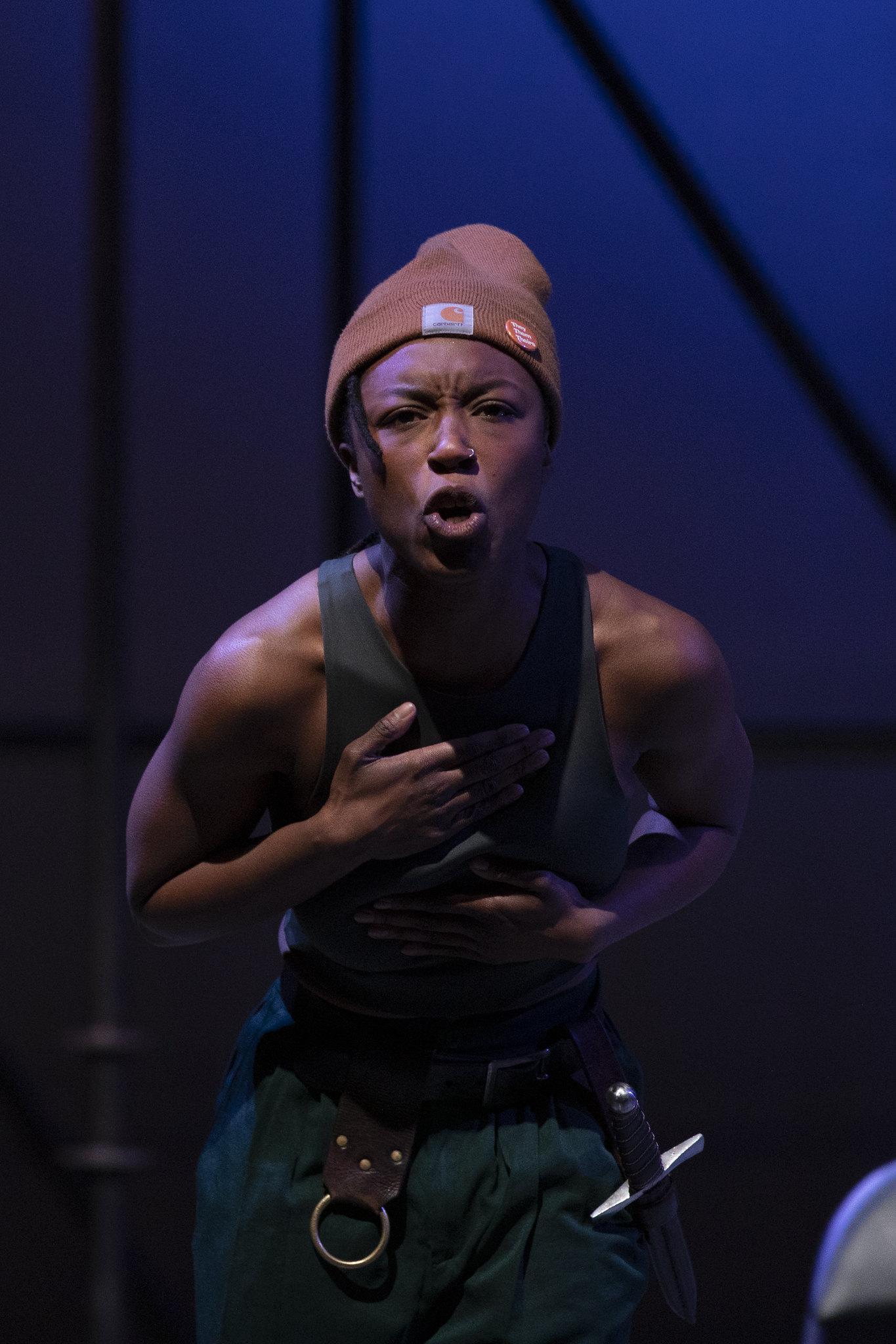 a black woman with a hat on a stage staring ahead. SHe has an intense look on her face.