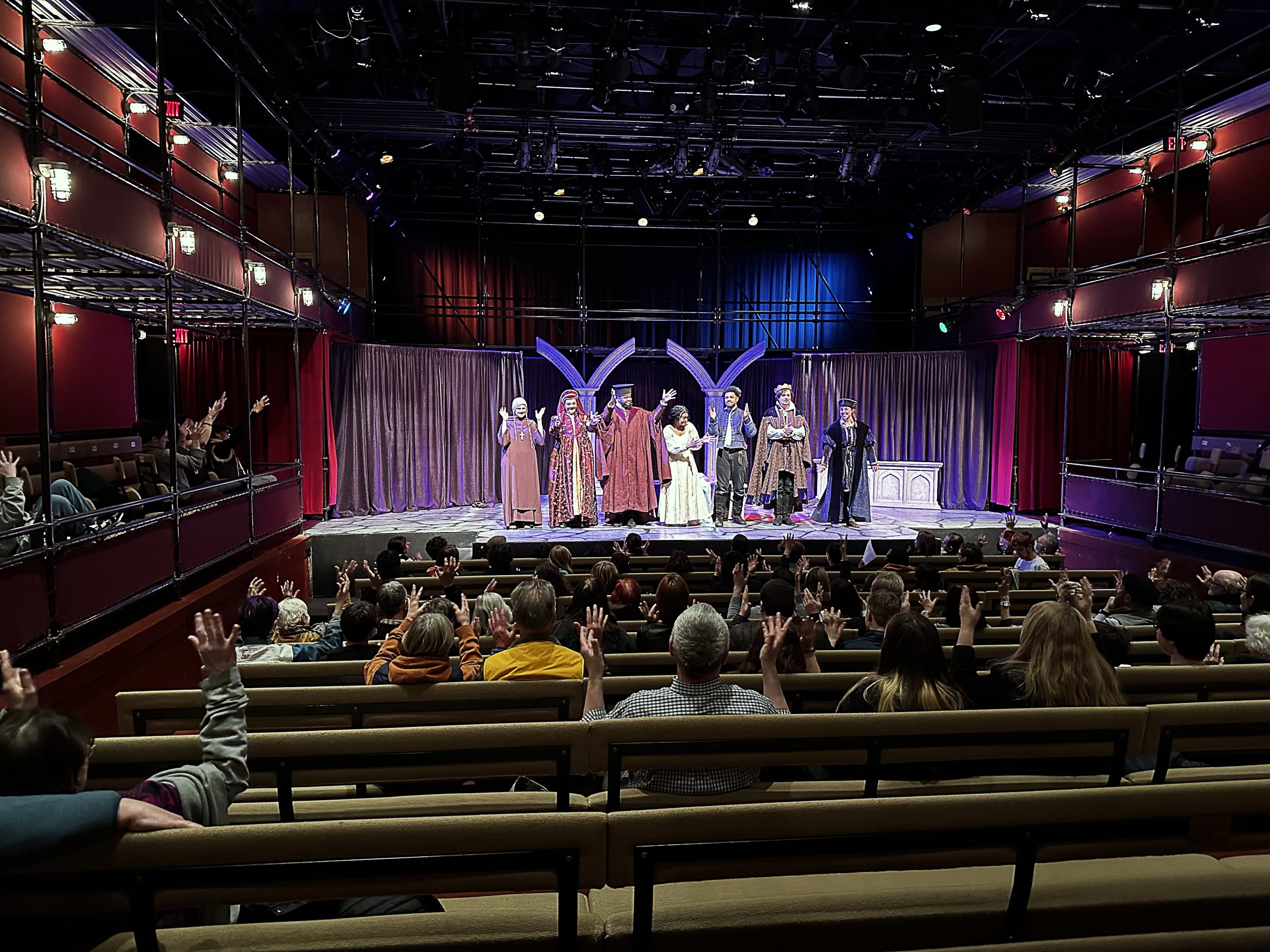 a photo of an audience n a theater, taken from the back of the house, which shows them clapping in a sesnory-friendly style with their hands in the air.