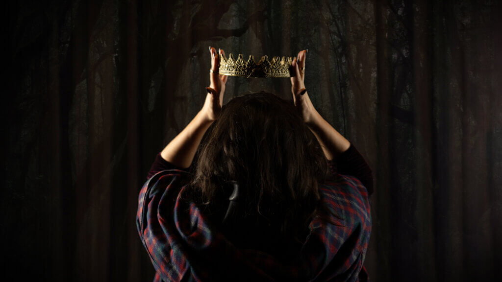 the back of a woman with black hair's head - she is raising a crown over her head