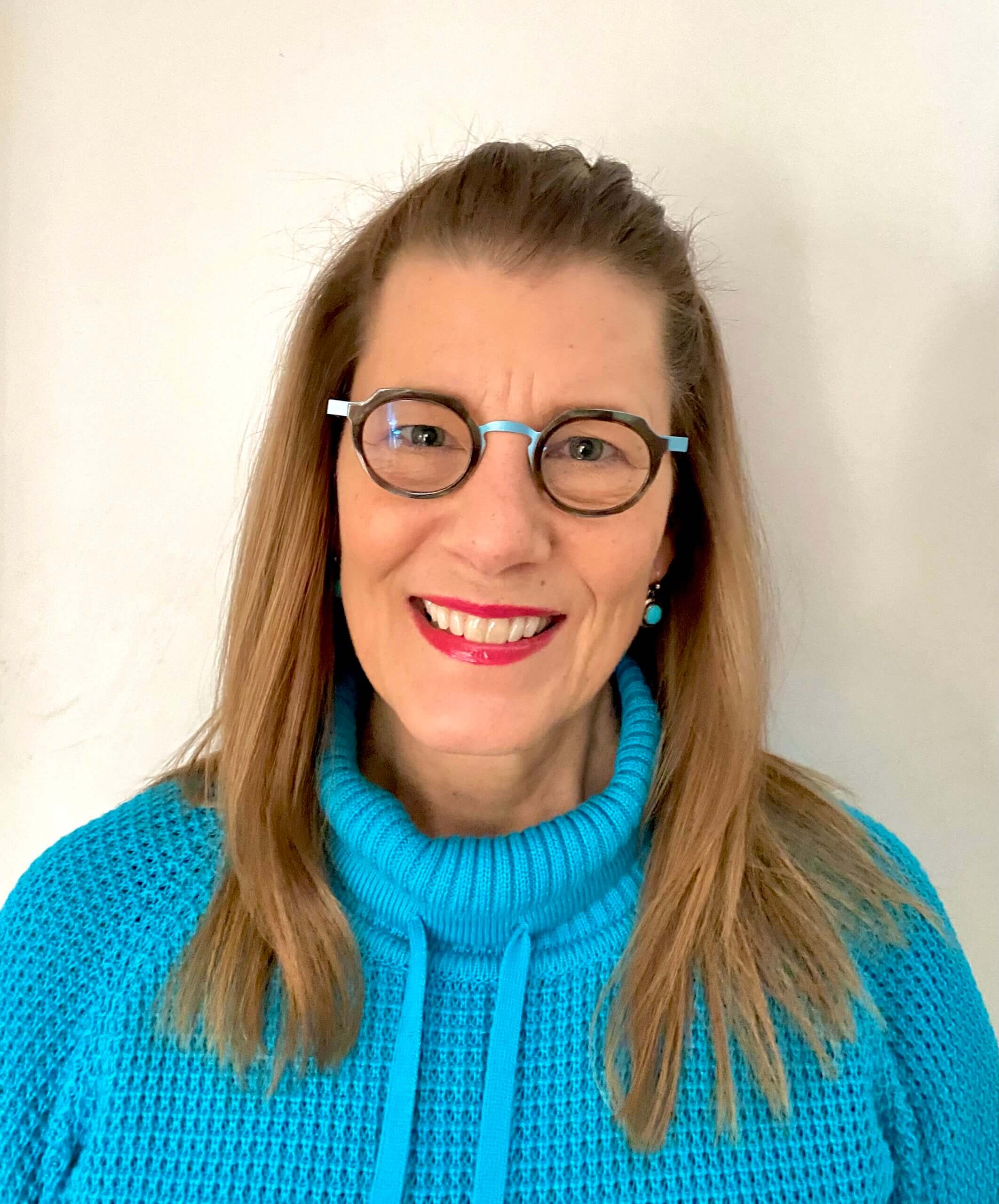 A woman with light brown hair, glasses, and a turquoise top smiling